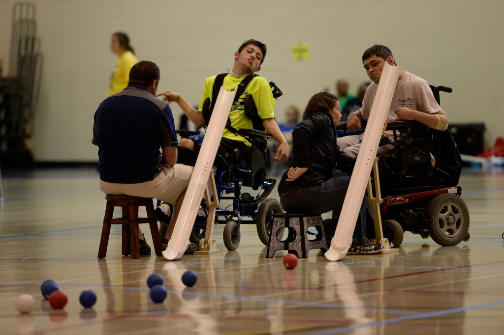 Two athletes in wheelchairs playing boccia with coaches sitting beside them