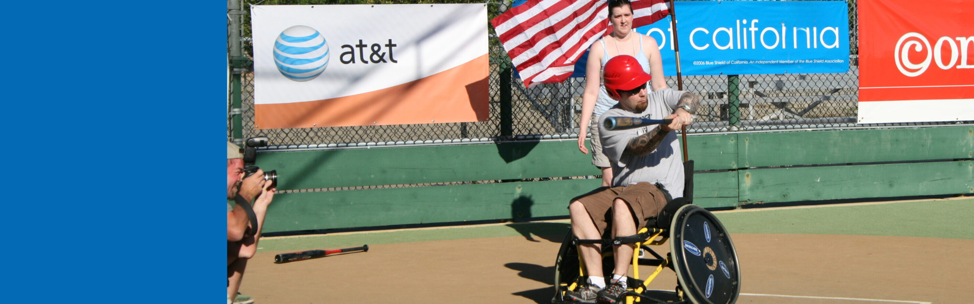 a person in a wheelchair on an outdoor baseball field, swinging the bat as a ball comes towards them