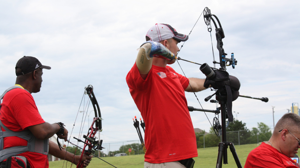 a person with a prosthetic arm is aiming an archery bow and preparing to release it