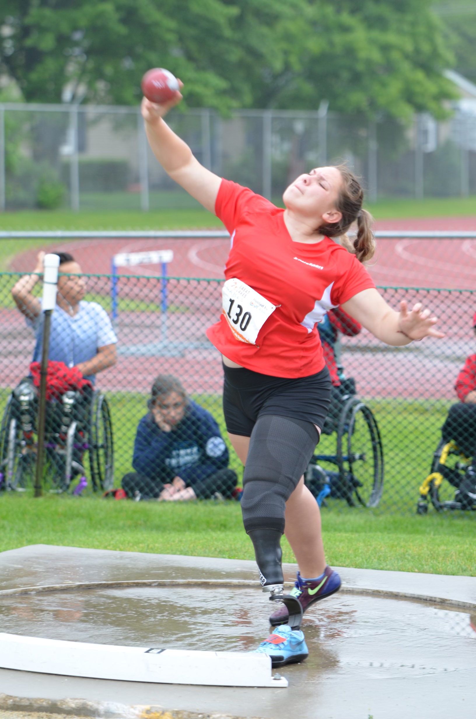 Female athlete with left leg below the knee amputation wearing a red shirt and throwing a ball
