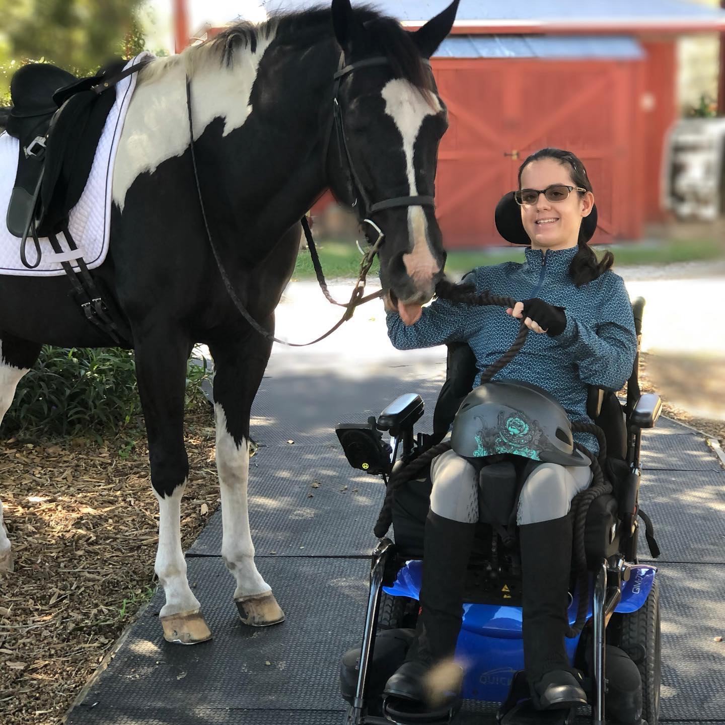 Female athlete in a wheelchair smiling at the camera and holding a lead rope with a horse posed beside her