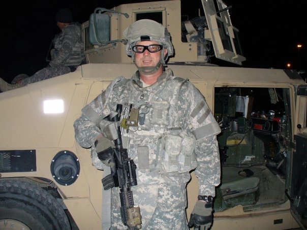 Male in military uniform standing in front of military vehicle smiling at camera