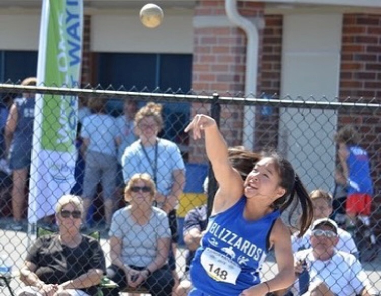 Female athlete wearing a blue shirt throwing a ball
