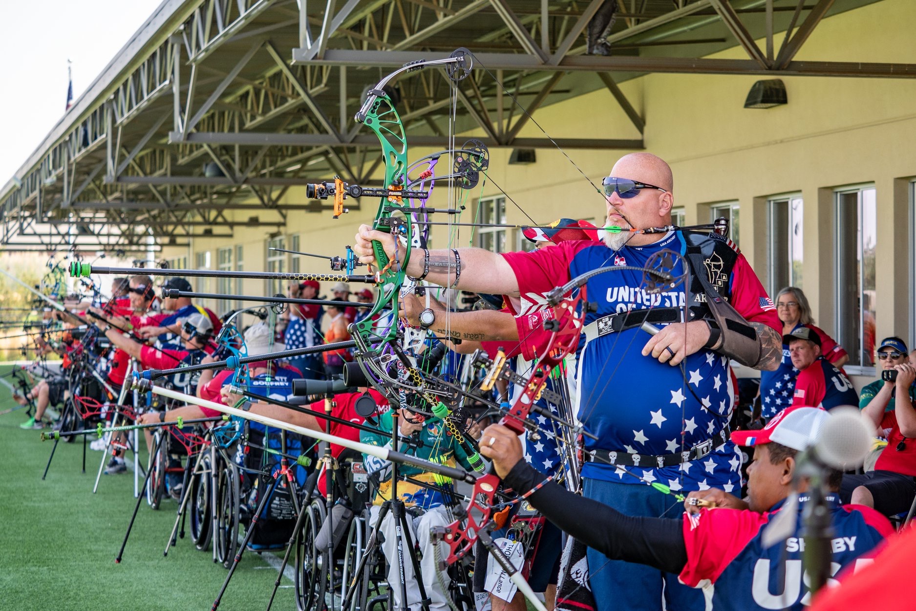 Multiple athletes using adaptive archery equipment and aiming towards targets off camera