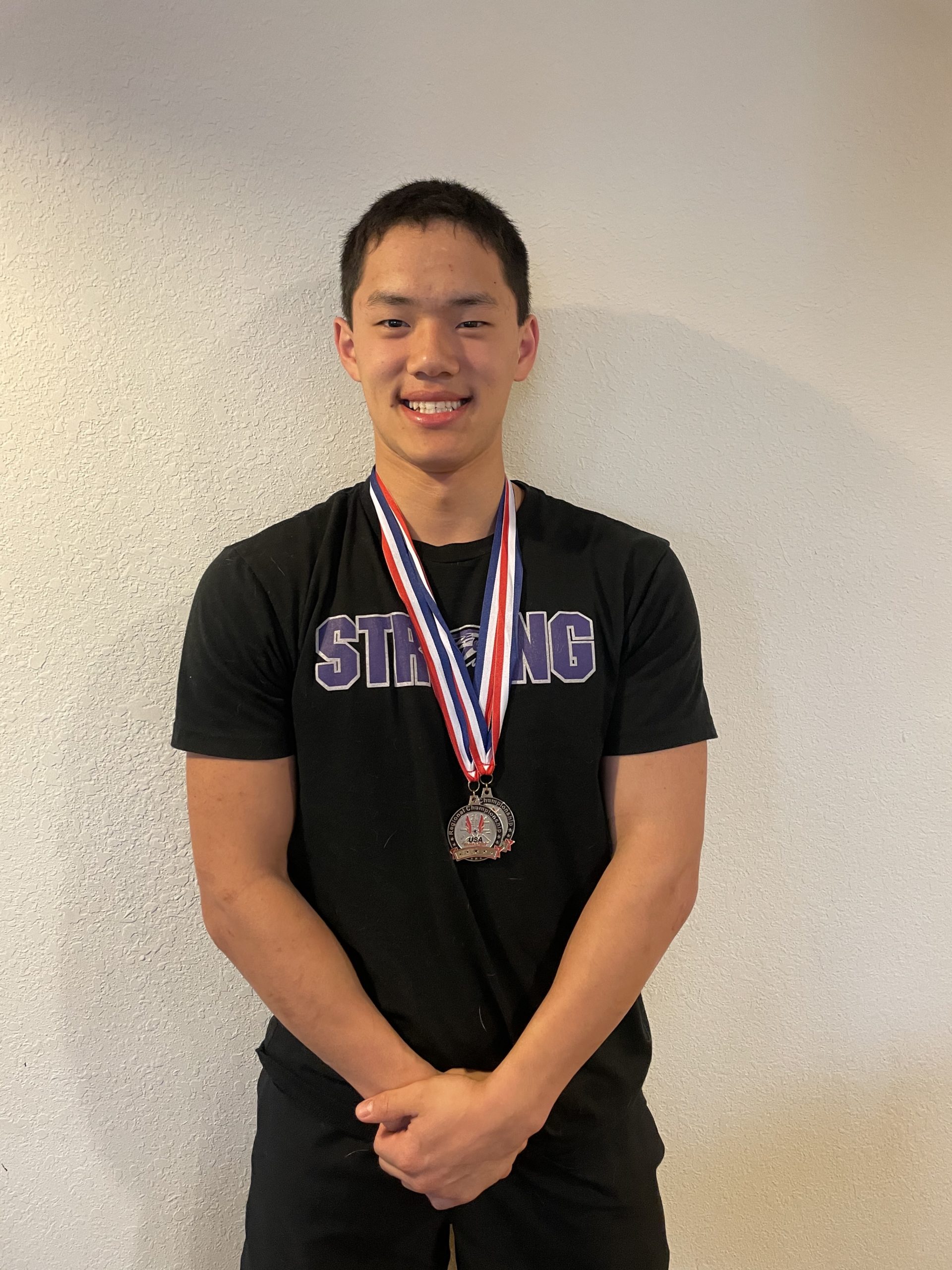 Male wearing a black shirt and two medals smiling at the camera
