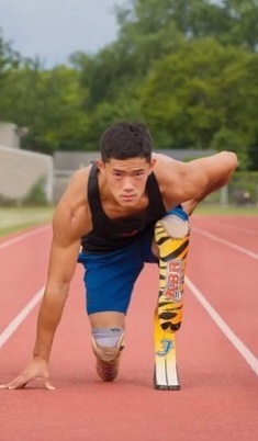 Male athlete with double below the knee amputation on one knee on a track looking up at the camera