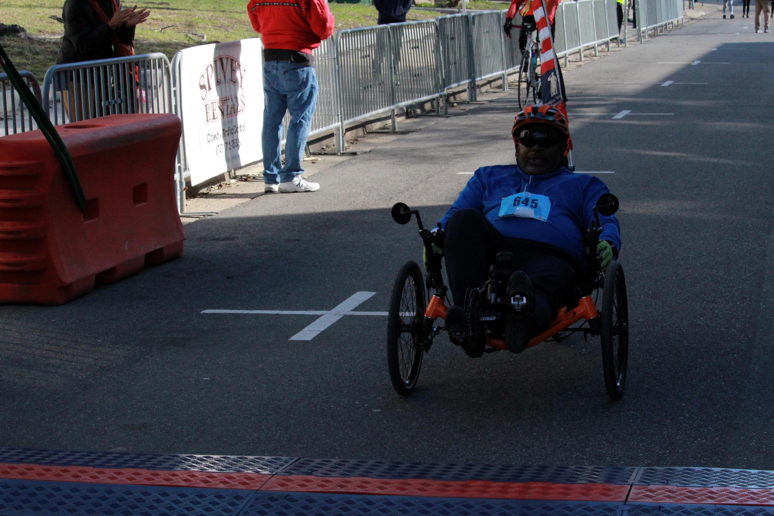Male in hand-cycling chair in a race about to cross an orange line