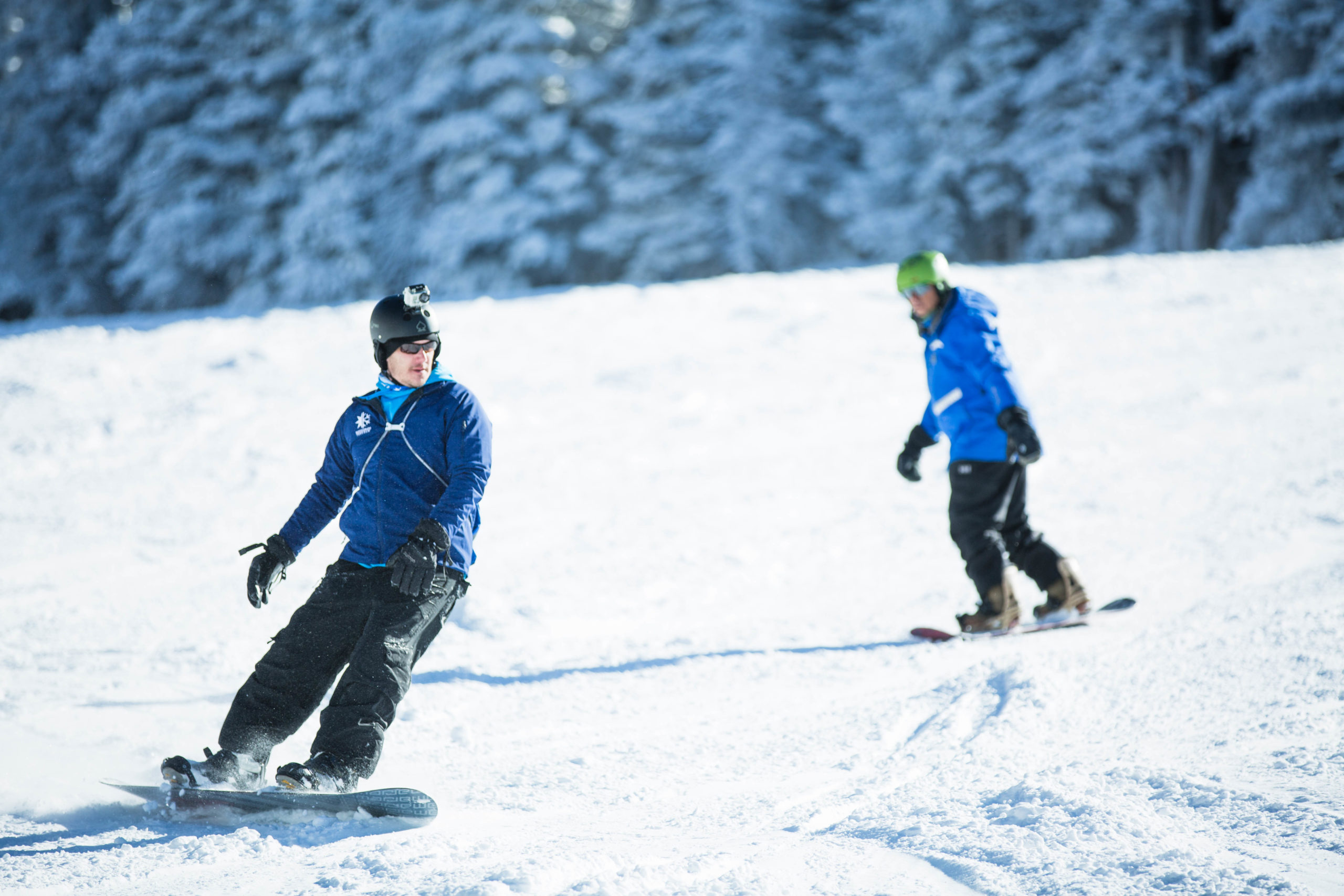 Two snowboarders wearing blue jackets and black pants snowboarding