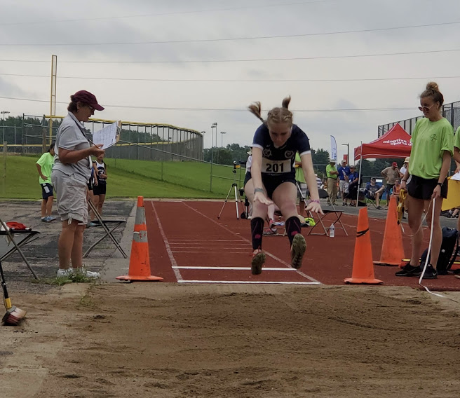 Female athlete midair performing long jump with other people onlooking