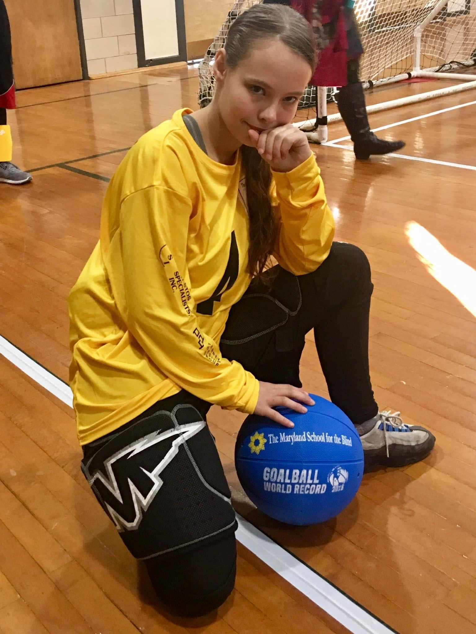 Female athlete kneeling on the ground with blue ball smiling at the camera