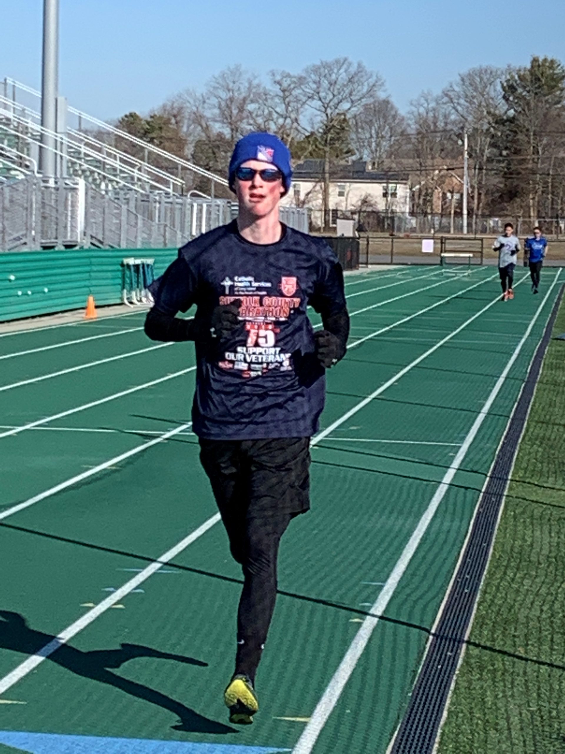 Male athlete wearing long sleeves and blue hat running on a track