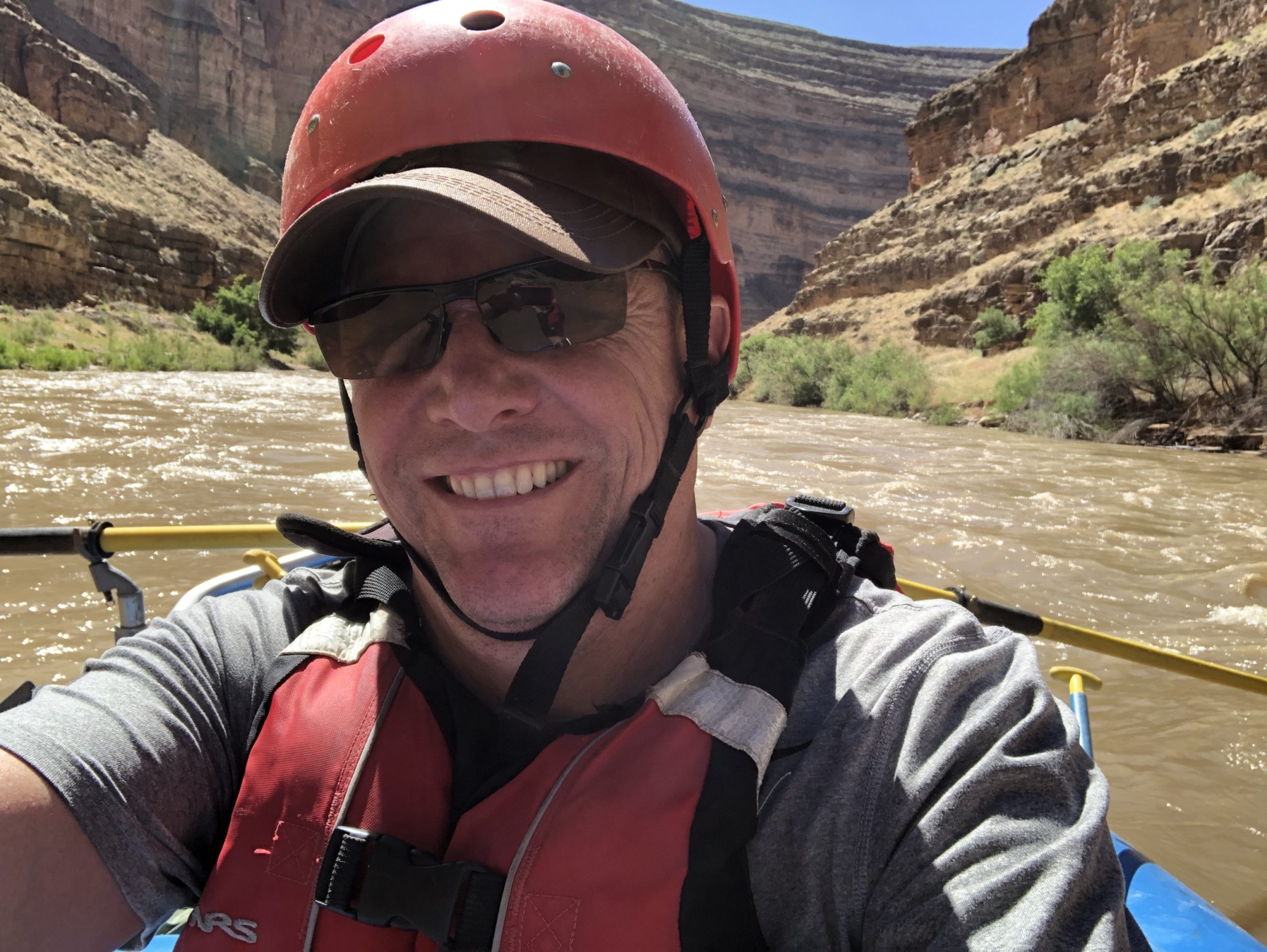 Male athlete on a boat in a river between two mountains smiling at the camera