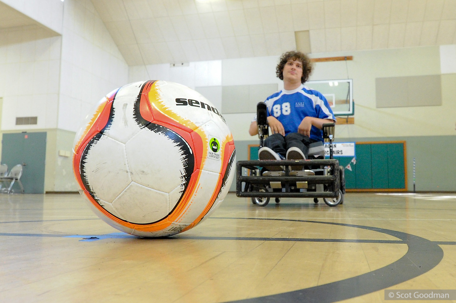 Soccer ball sitting on gymnasium floor with male athlete in a wheelchair smiling at the camera