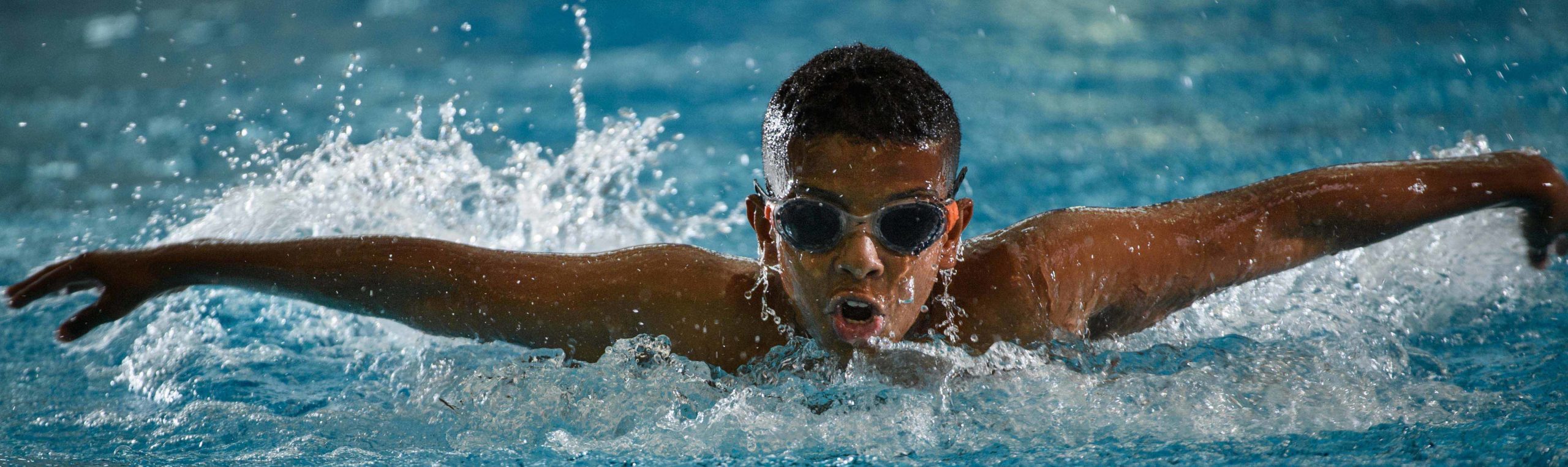 Male athlete wearing goggles swimming and coming out of water for air