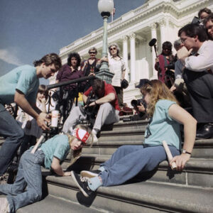 People with disabilities crawling up the capitol stairs with crowd of people and media watching