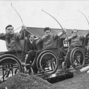 Black and white photo of three male athletes in wheelchairs doing archery