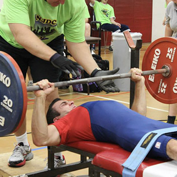 male athlete lifting weight over his head with weight spotter standing behind him