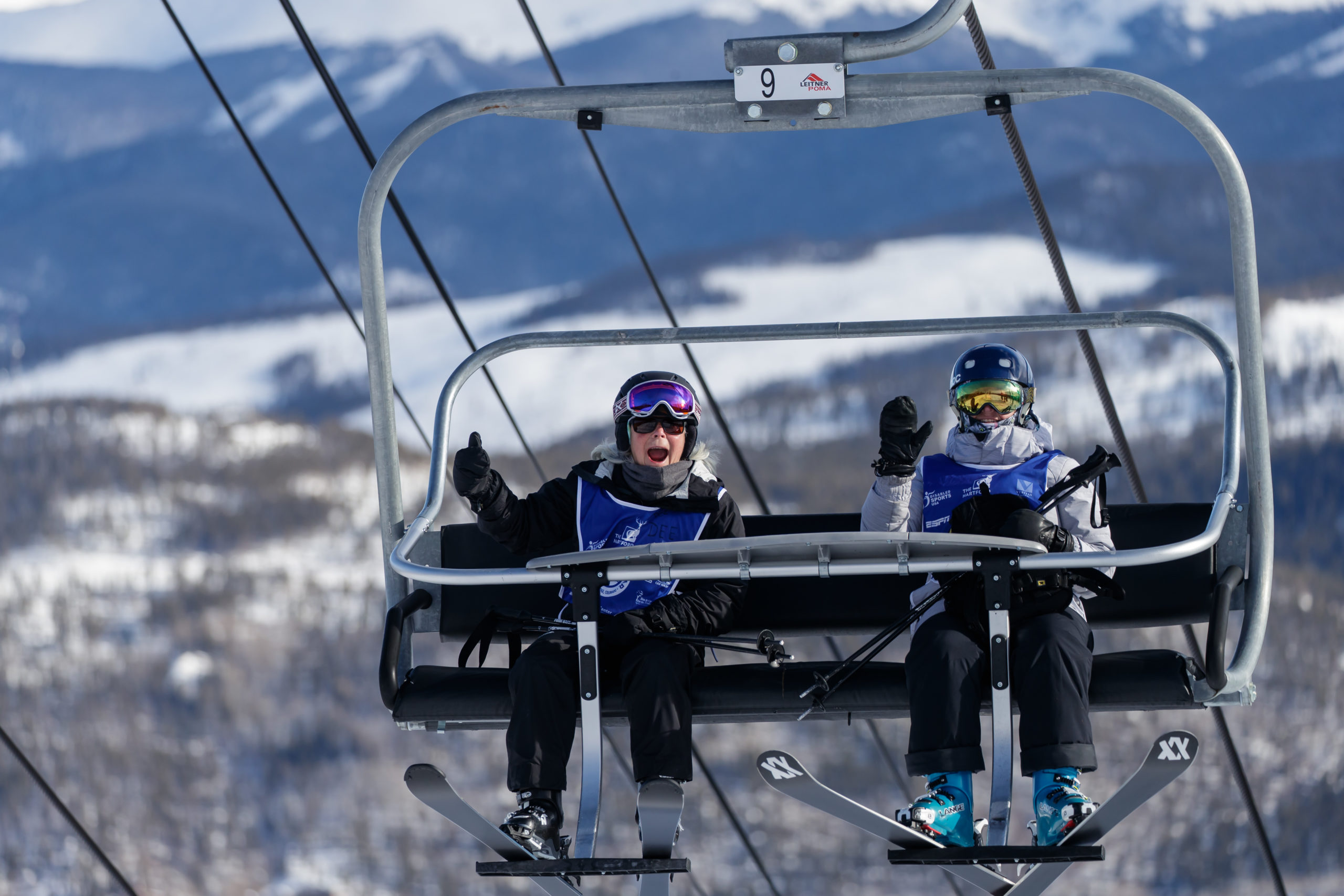 Two Ski Spec participants riding the Breckenridge Ski Resort lift and waving to the camera