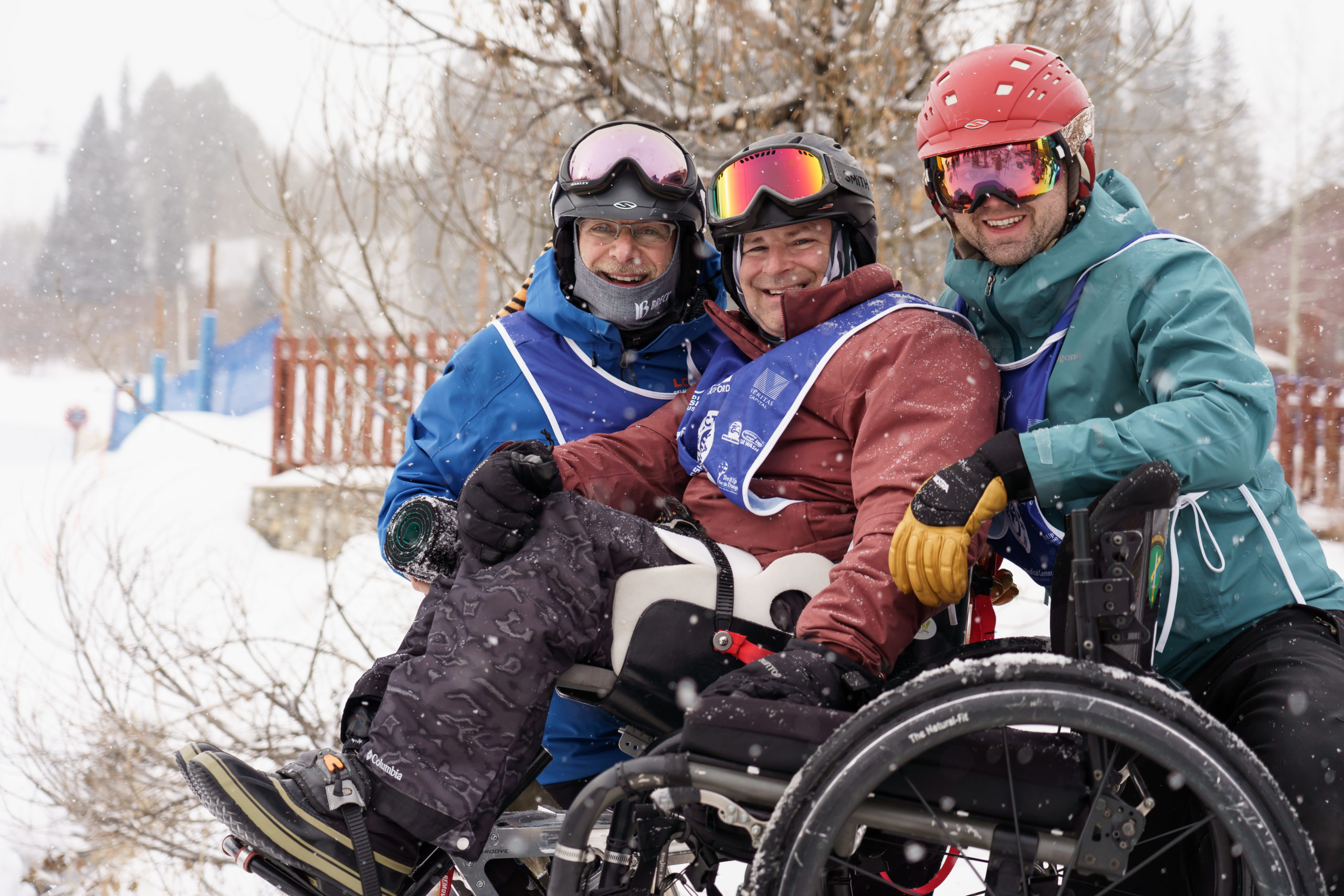 Two Ski Spec coaches with athlete in a wheelchair smiling at camera