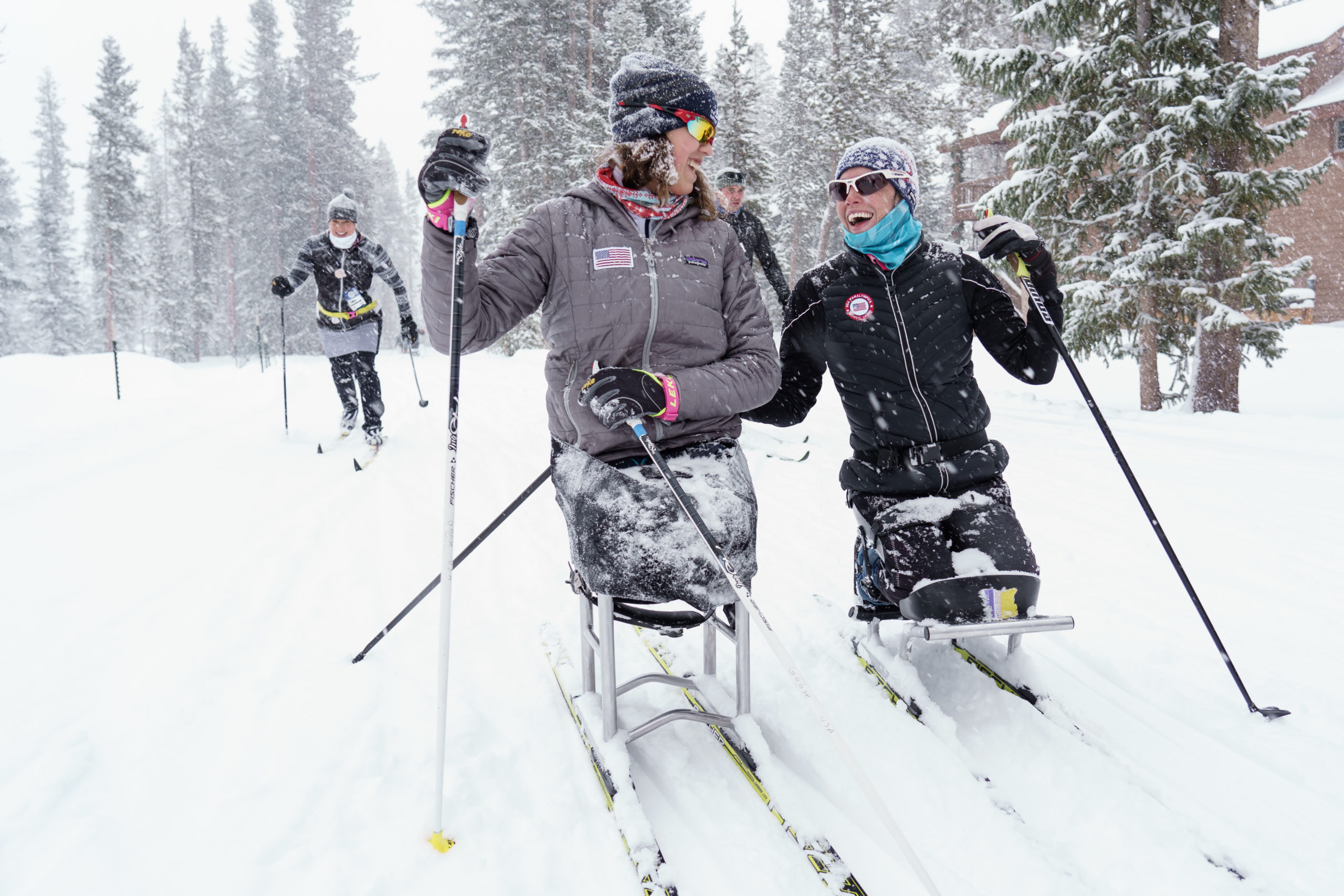 Ski Spec athletes on bi-skis skiing down slope smiling at each other
