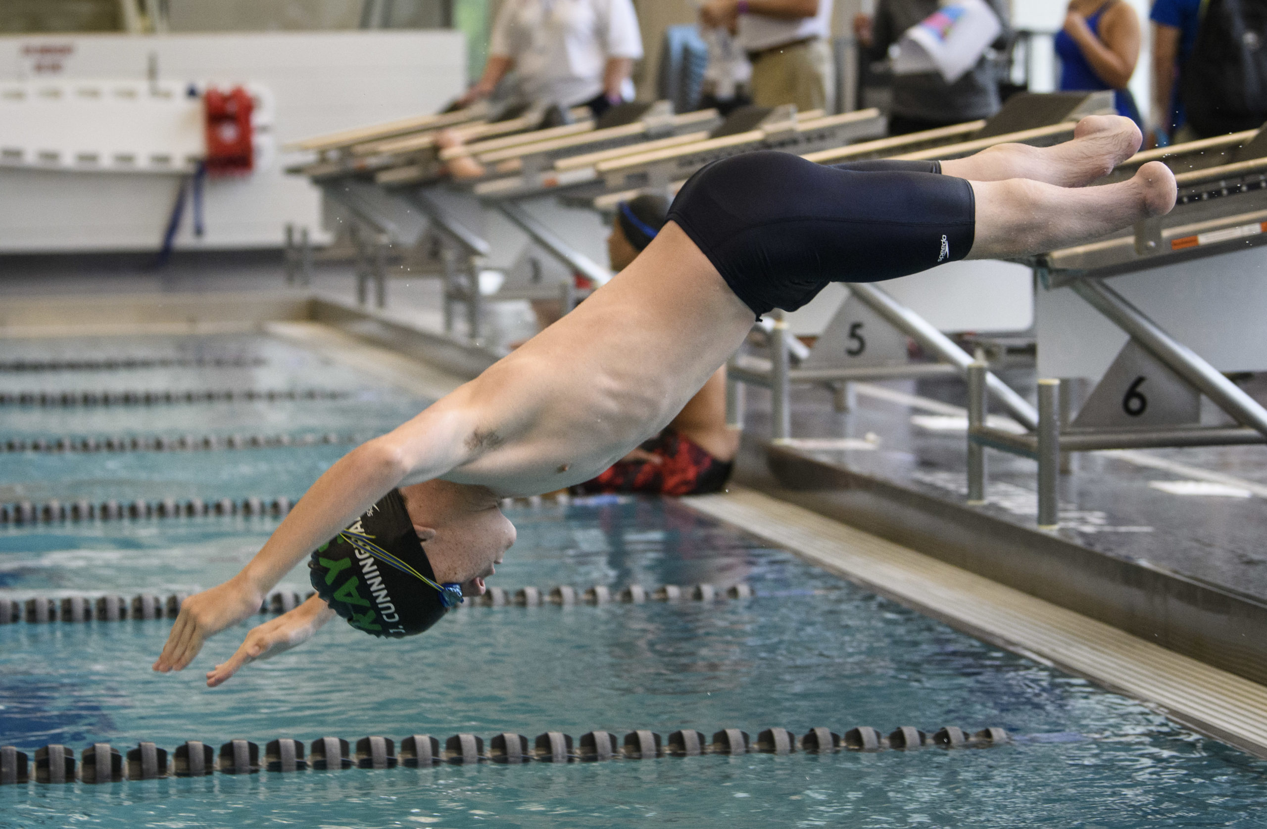 Male athlete with double leg amputation diving off of diving block into the swimming pool