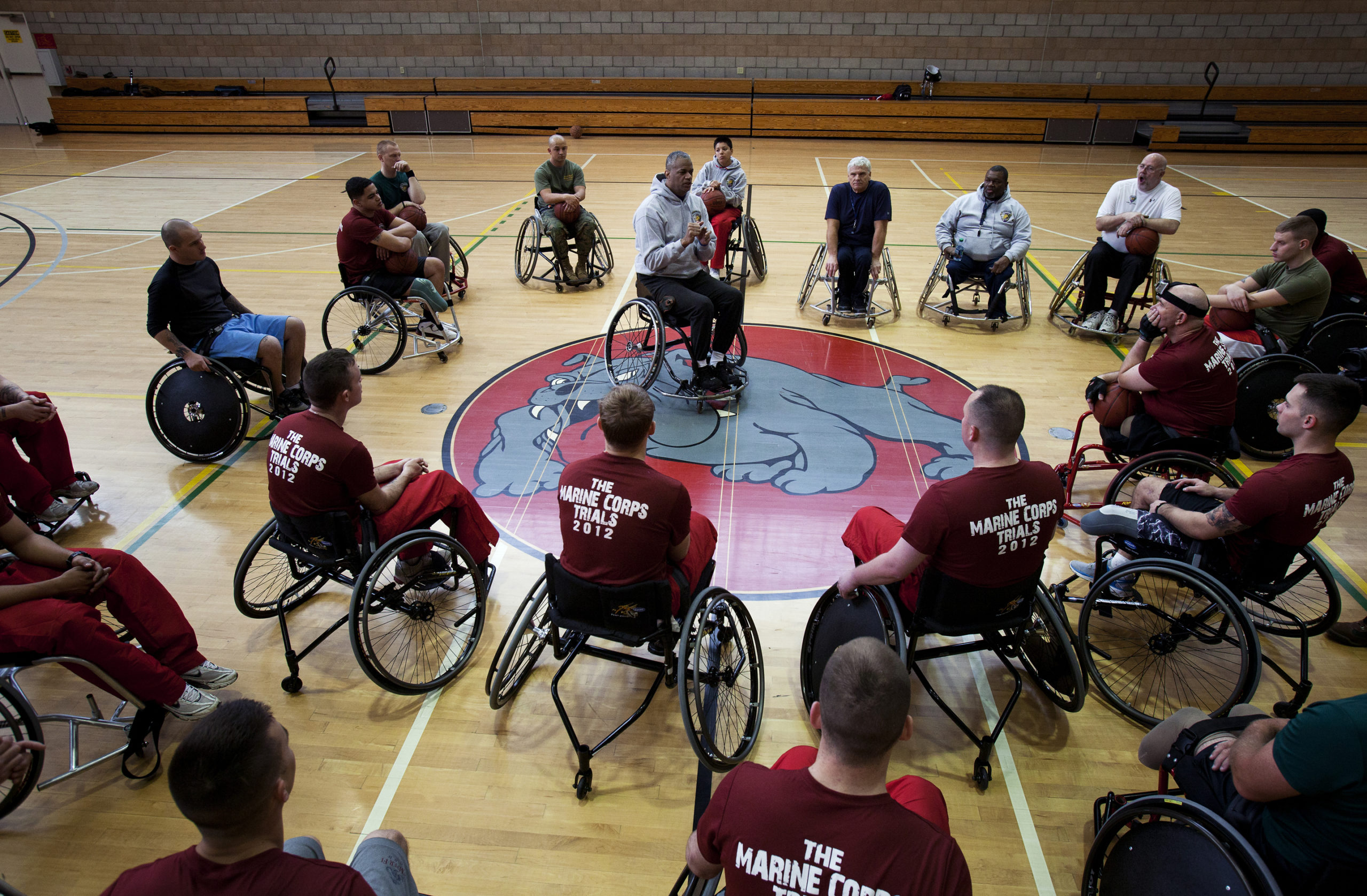 Group of athletes in wheelchairs in a circle listening to another athlete in the middle of the circle speaking