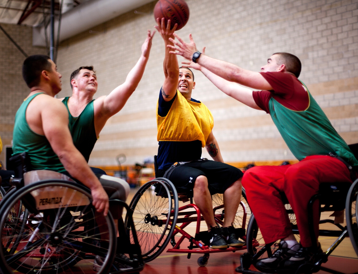 Four athletes in wheelchairs reaching for a basketball