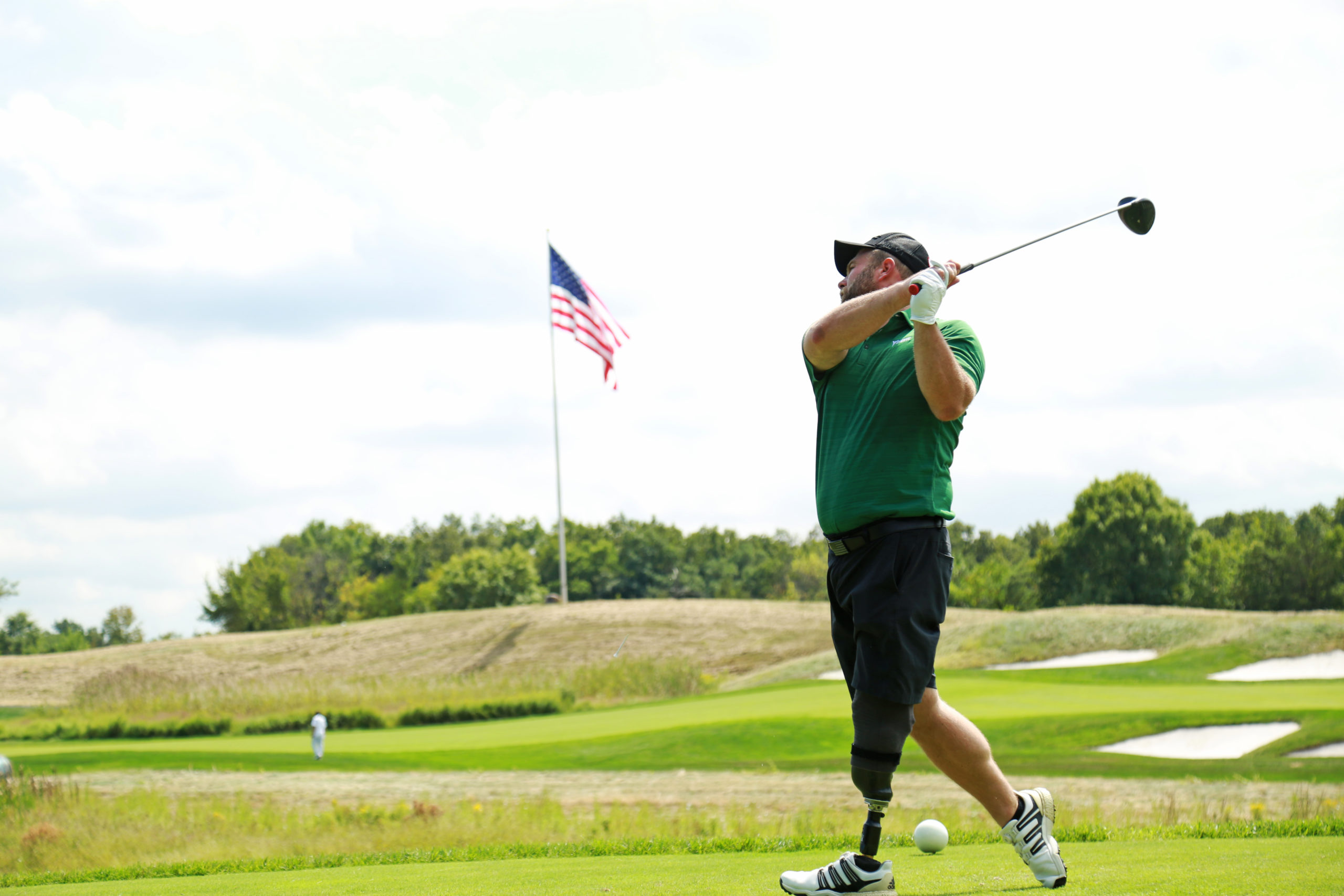 Leg amputee golfer swinging with US flag in background