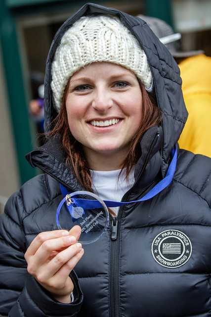 Female in USA Paralympics Snowboarding coat holding a medal and smiling at the camera