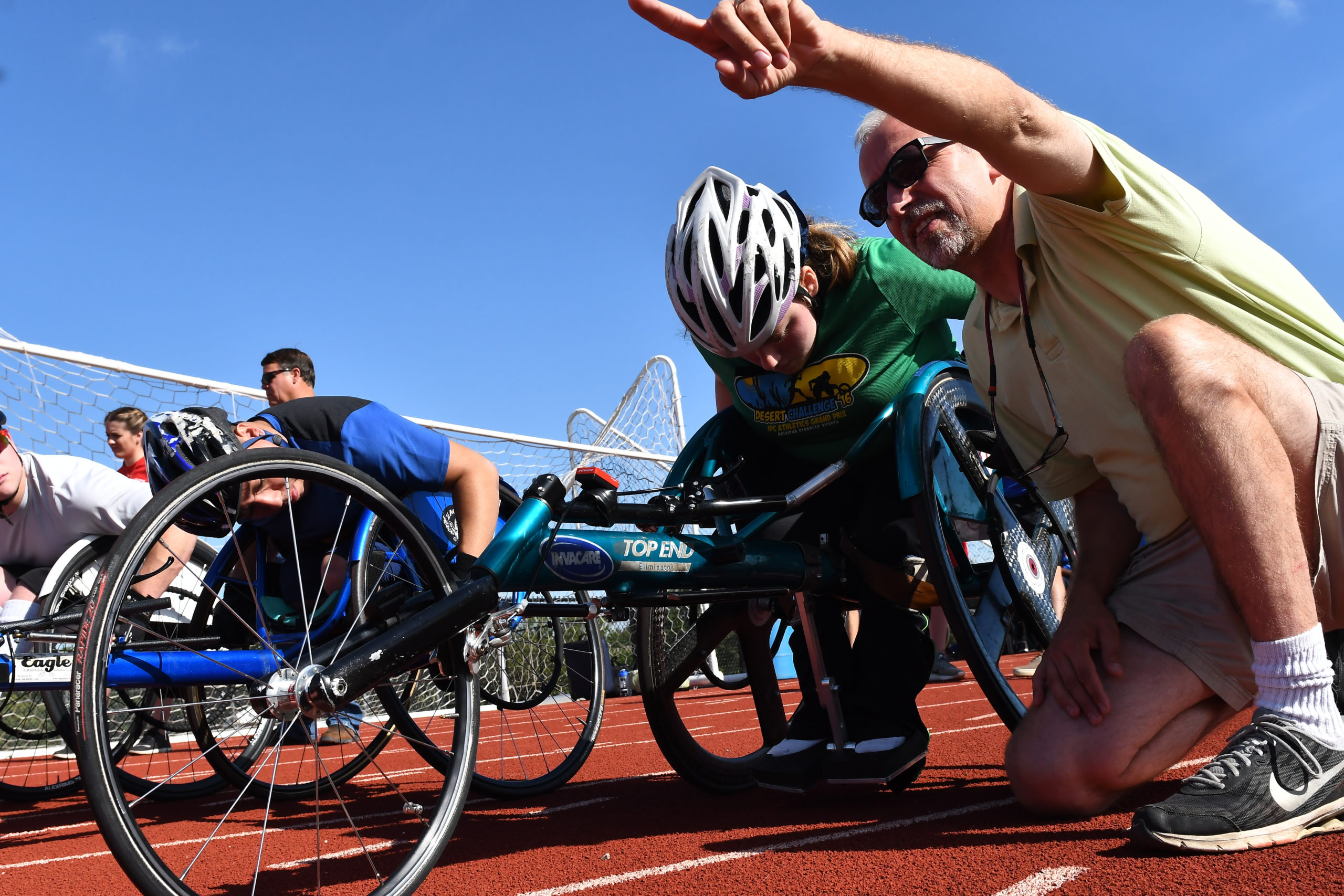 Athlete in a racing wheelchair with a coach kneeling on the ground and pointing