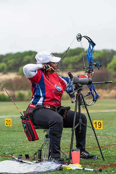 Female seated athlete preparing to shoot an arrow with bow drawn back