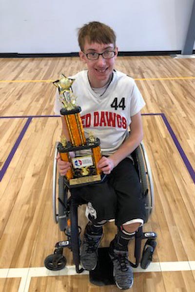 Male athlete in a wheelchair smiling at camera and holding a trophy