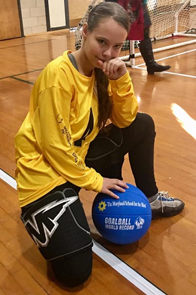 Female athlete kneeling on the ground with blue ball smiling at the camera