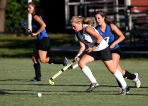 Female athletes running on a field playing field hockey