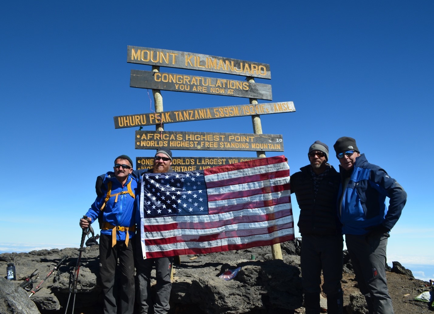 Three athletes holding an American flag at the top of a hike.