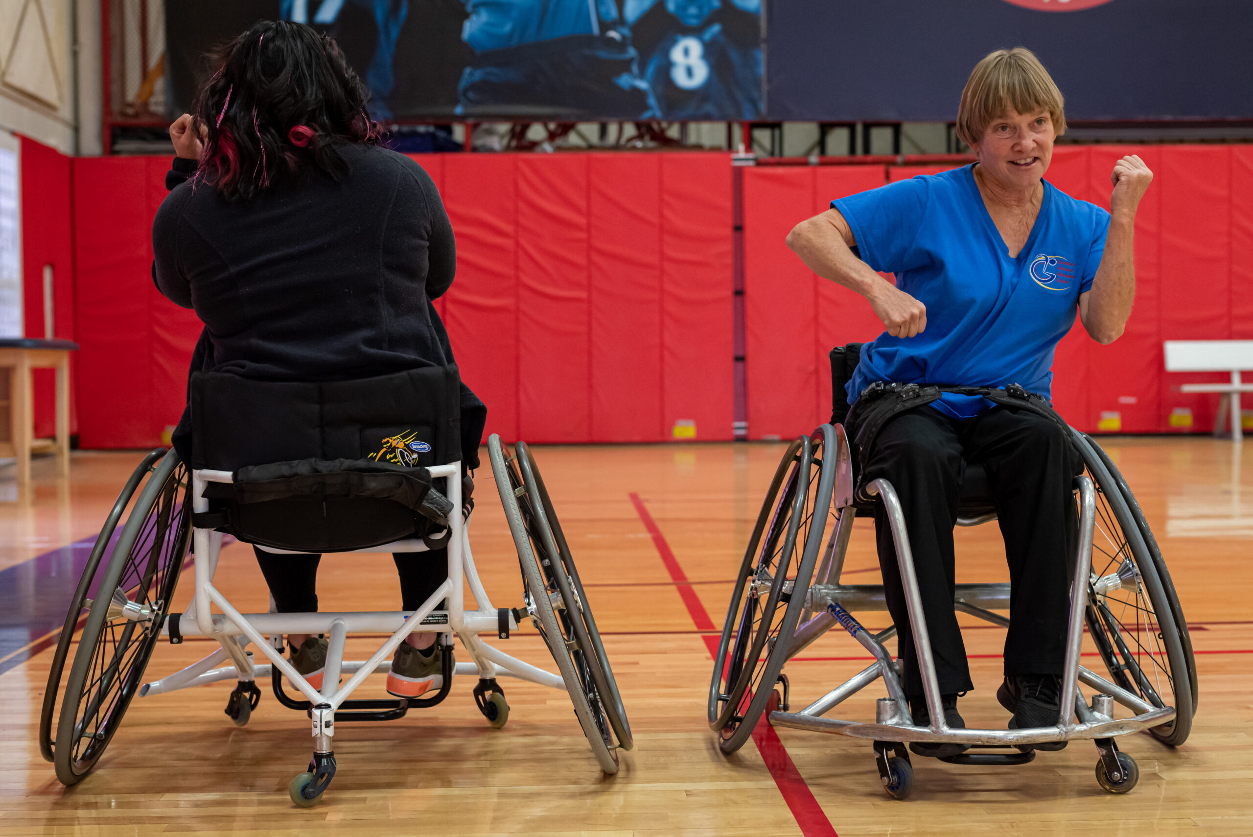 Two people in wheelchairs smiling and pounding their fists together