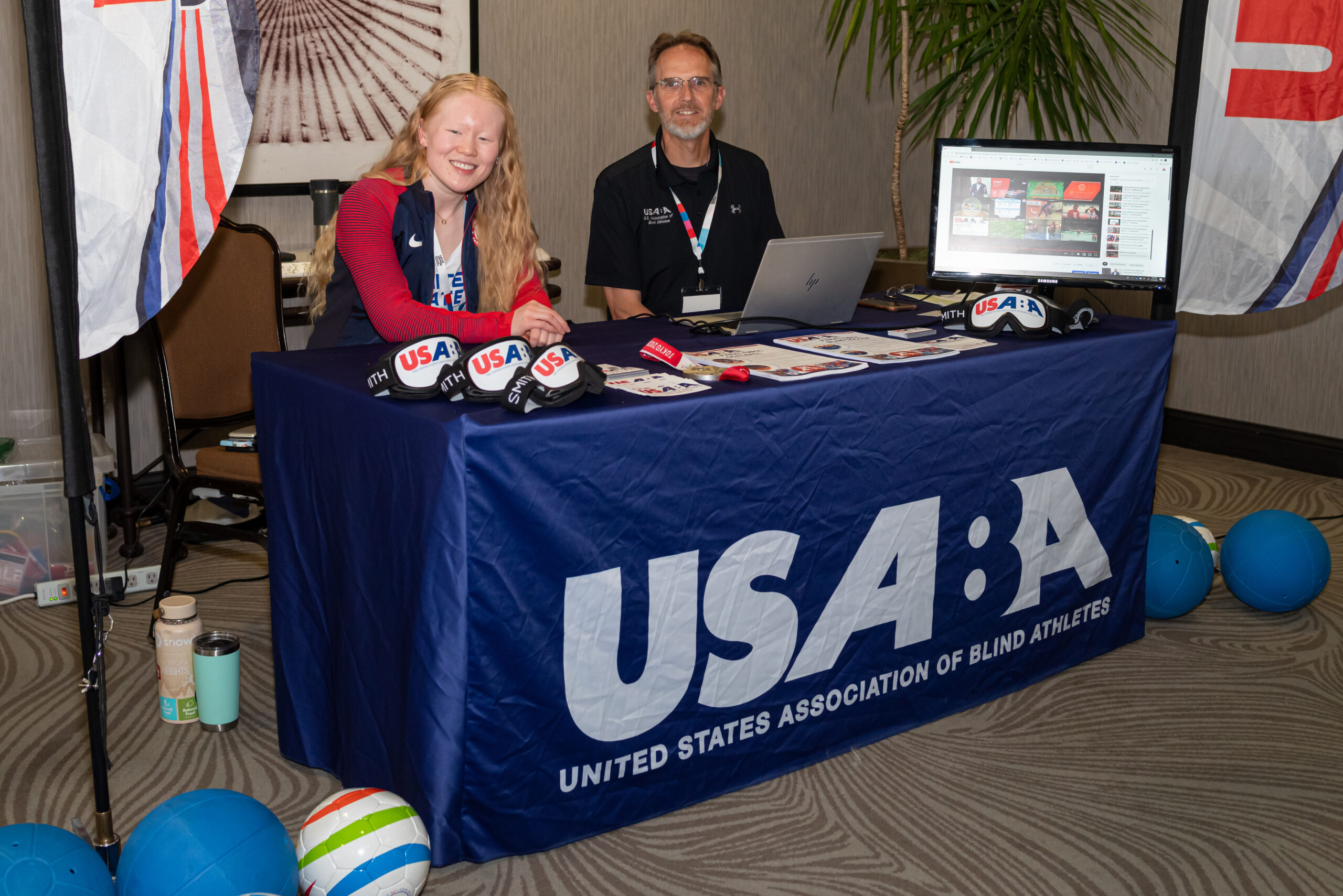 2 USABA representatives smiling at camera from behind USABA vendor table
