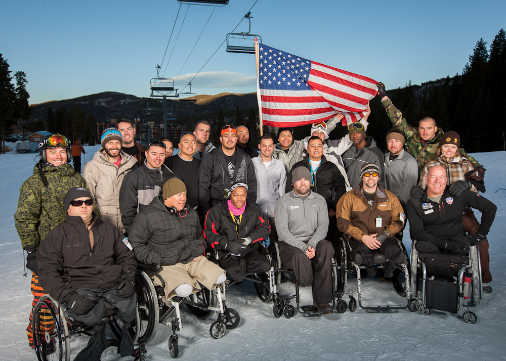 Group of warfighters posing for a picture on the snow with an American flag.
