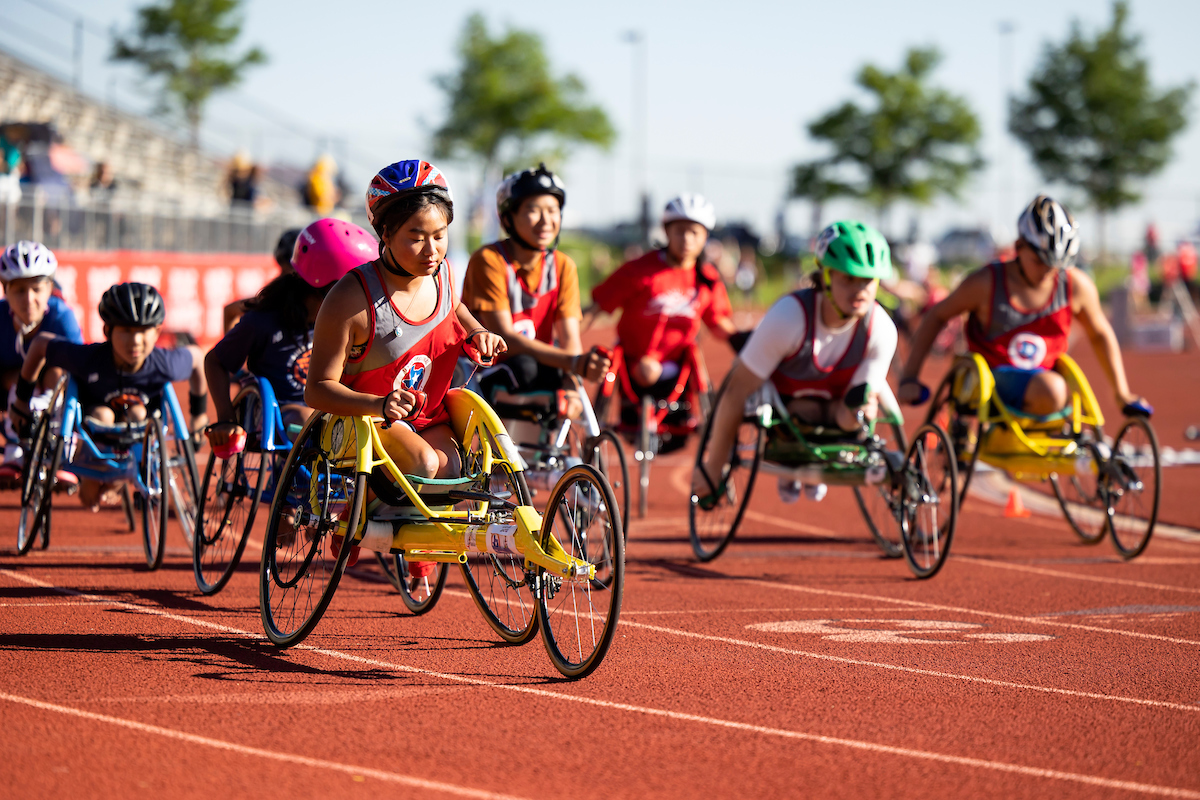 Big group of people participating in wheelchair racing on an outdoor track