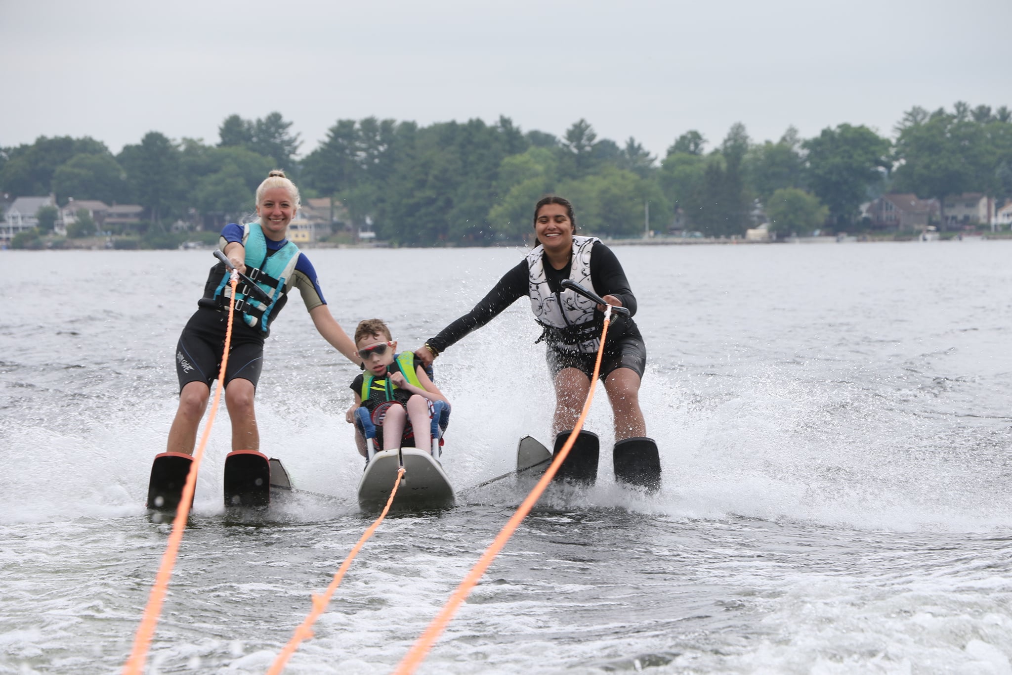 Two people standing on water skis and a person in the middle on a sit water ski