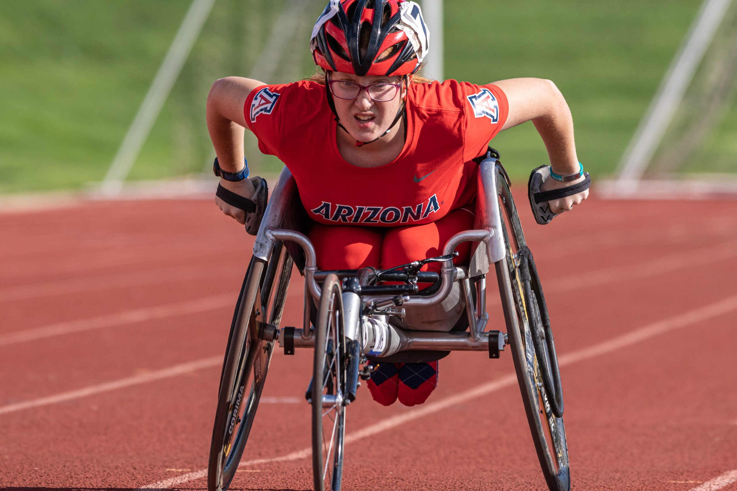 Athlete on a track in a racing wheelchair. Athlete is wearing all red University of Arizona uniform on