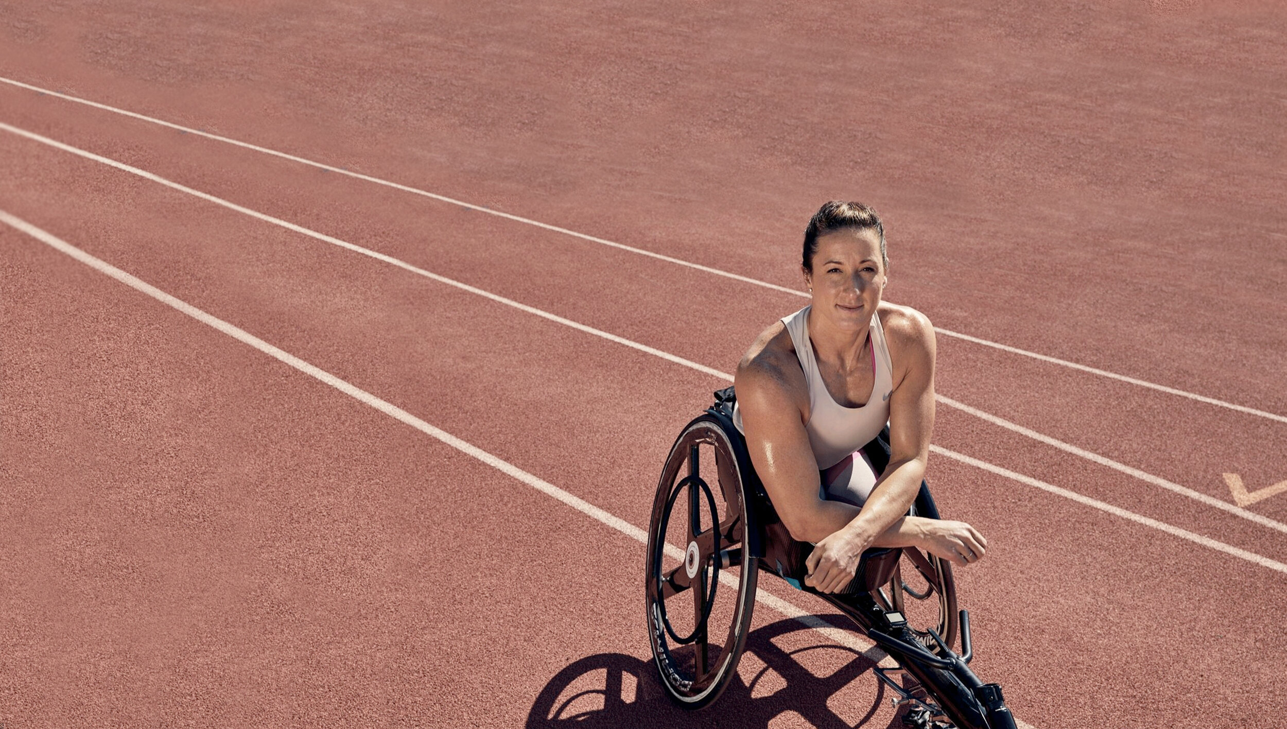 Tatyana McFadden sitting in a racing wheelchair on a track looking up at camera.