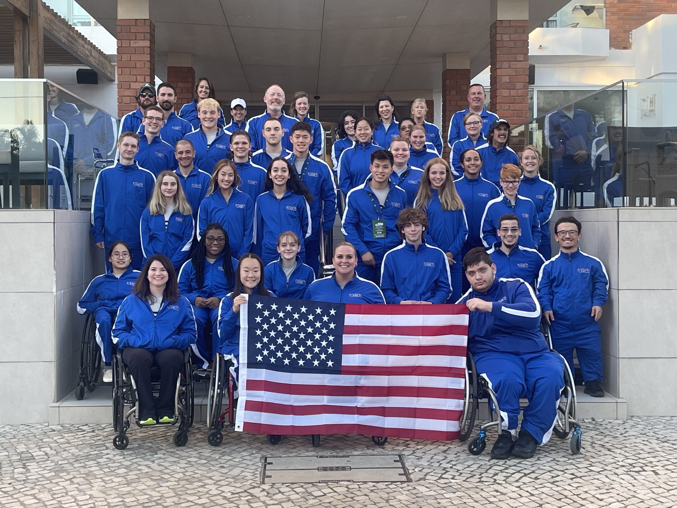 Group of athletes and staff wearing USA uniform posed on stairs with USA flag