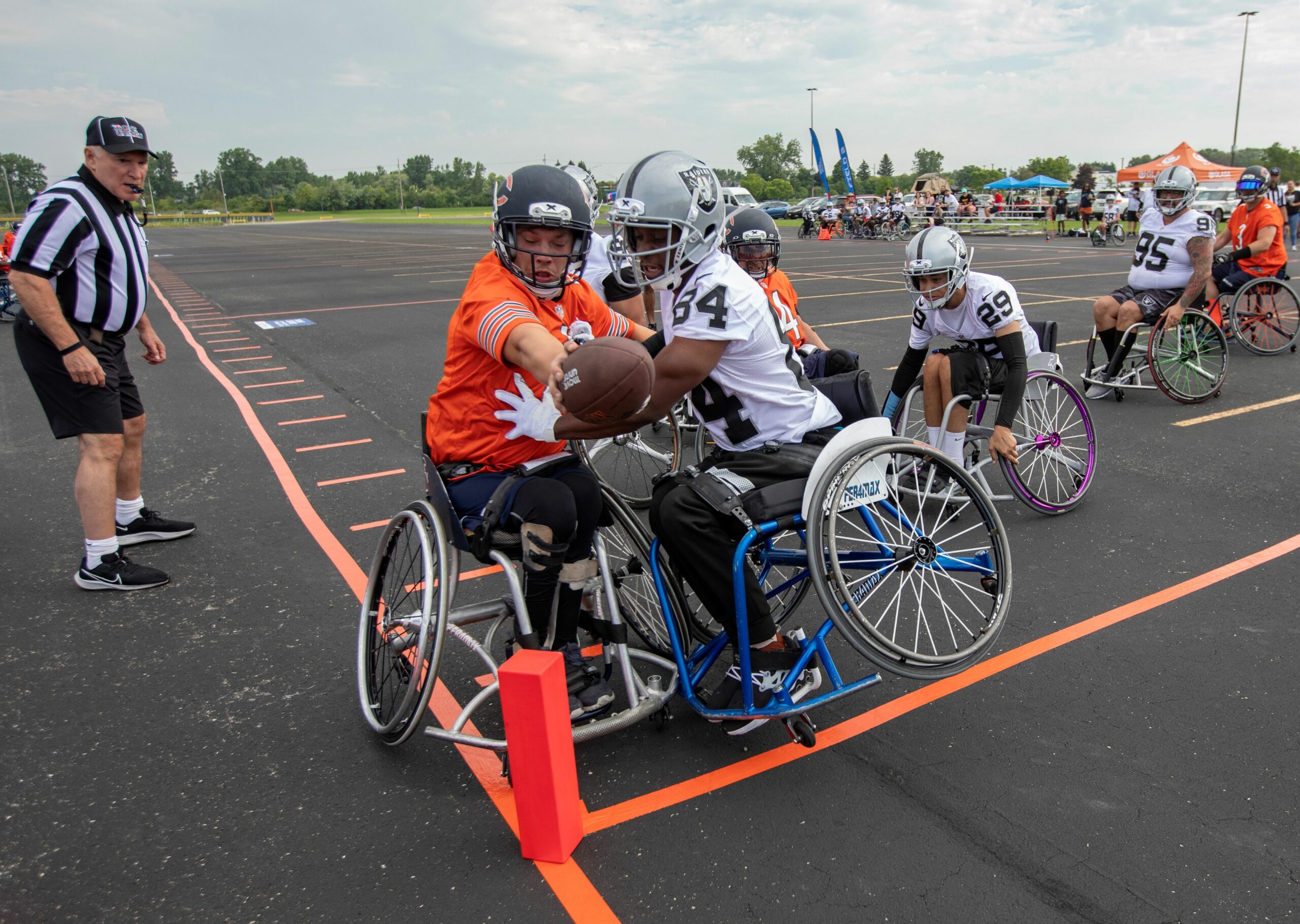 A wheelchair football player reaches across the end zone with the ball as a defender approaches