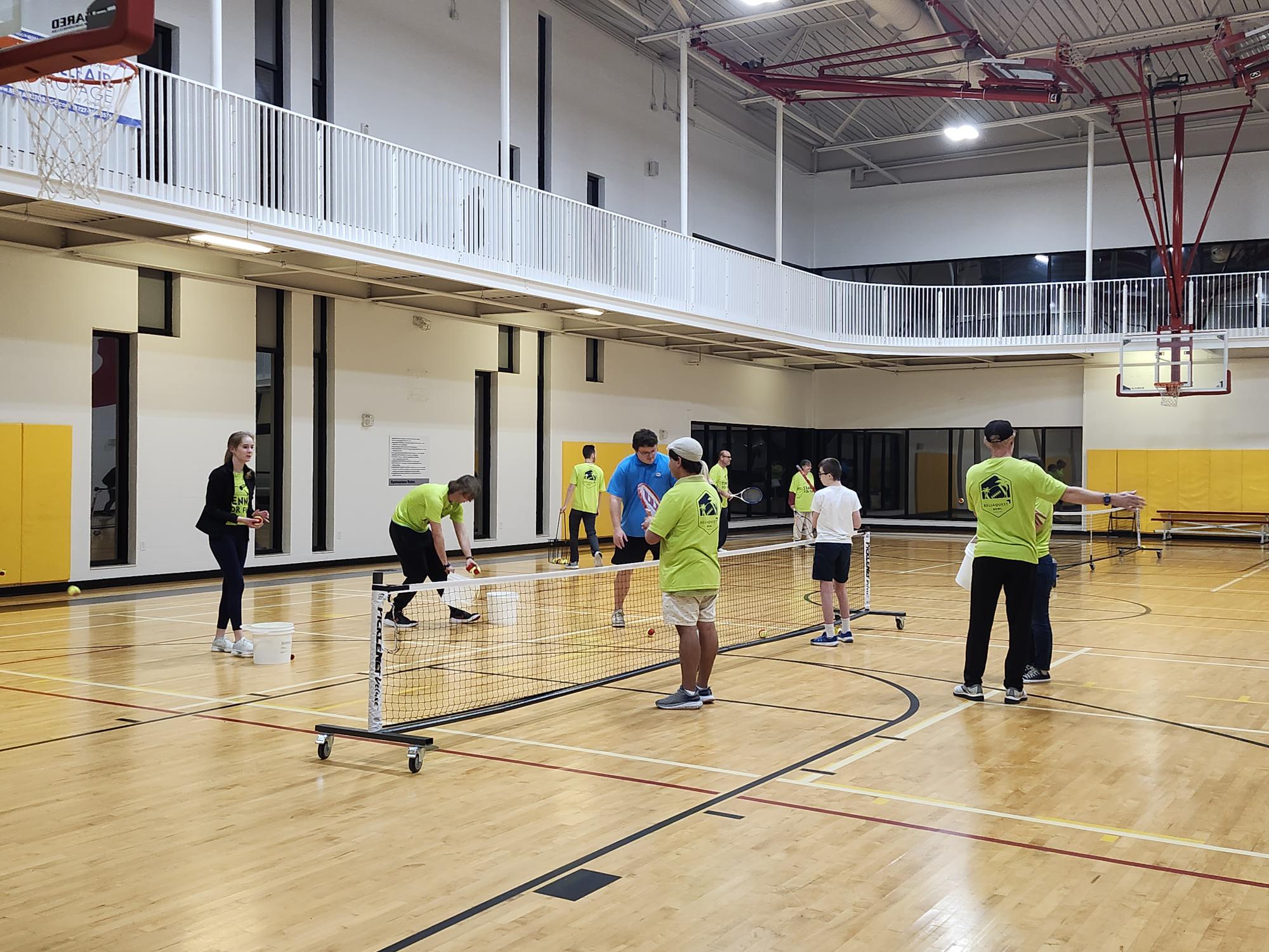 A group of individuals practice tennis in a gym