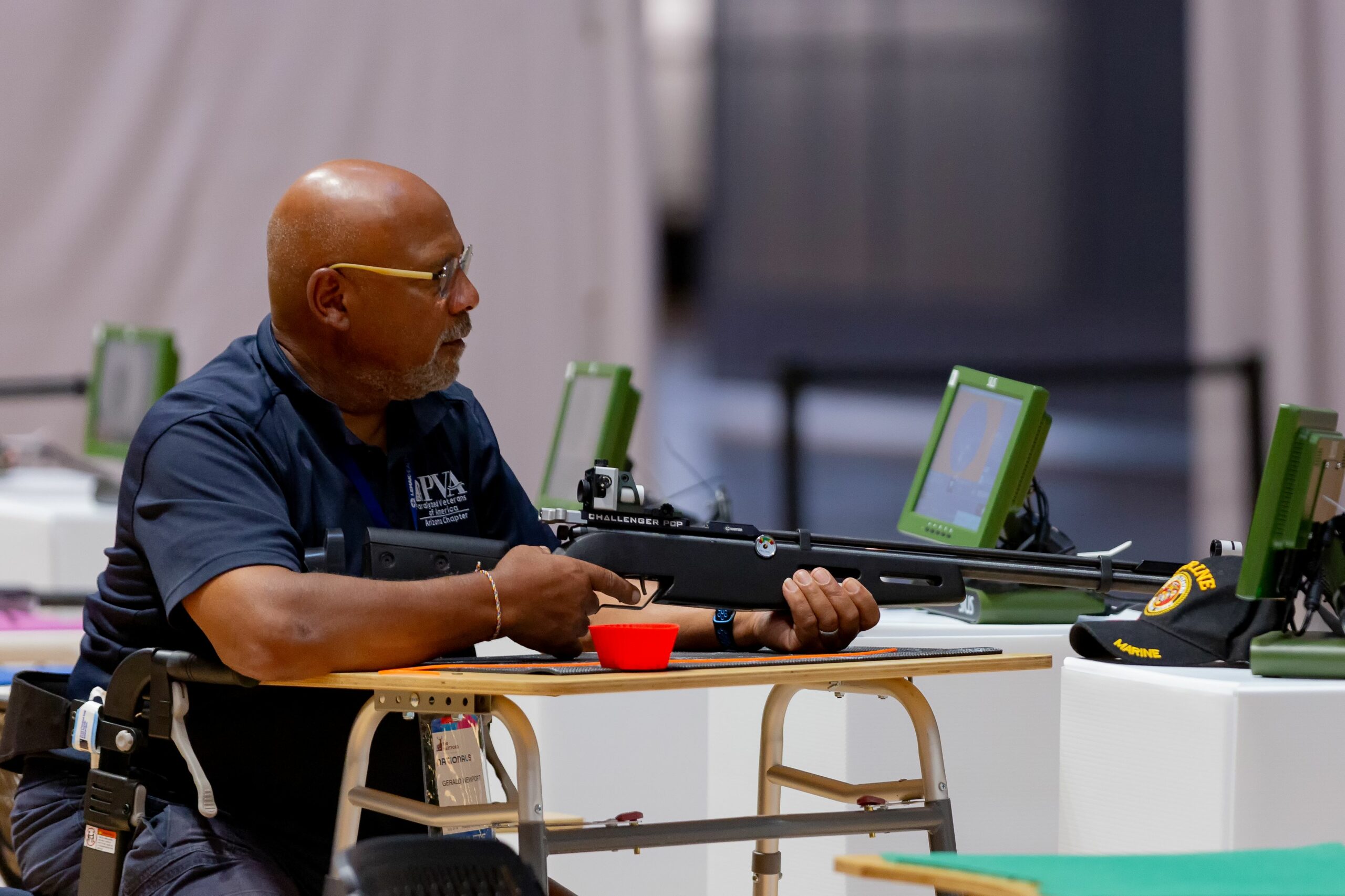 Athlete at air rifle competition. Athlete is seated with table in front of them and air pistol in hand resting on the table.