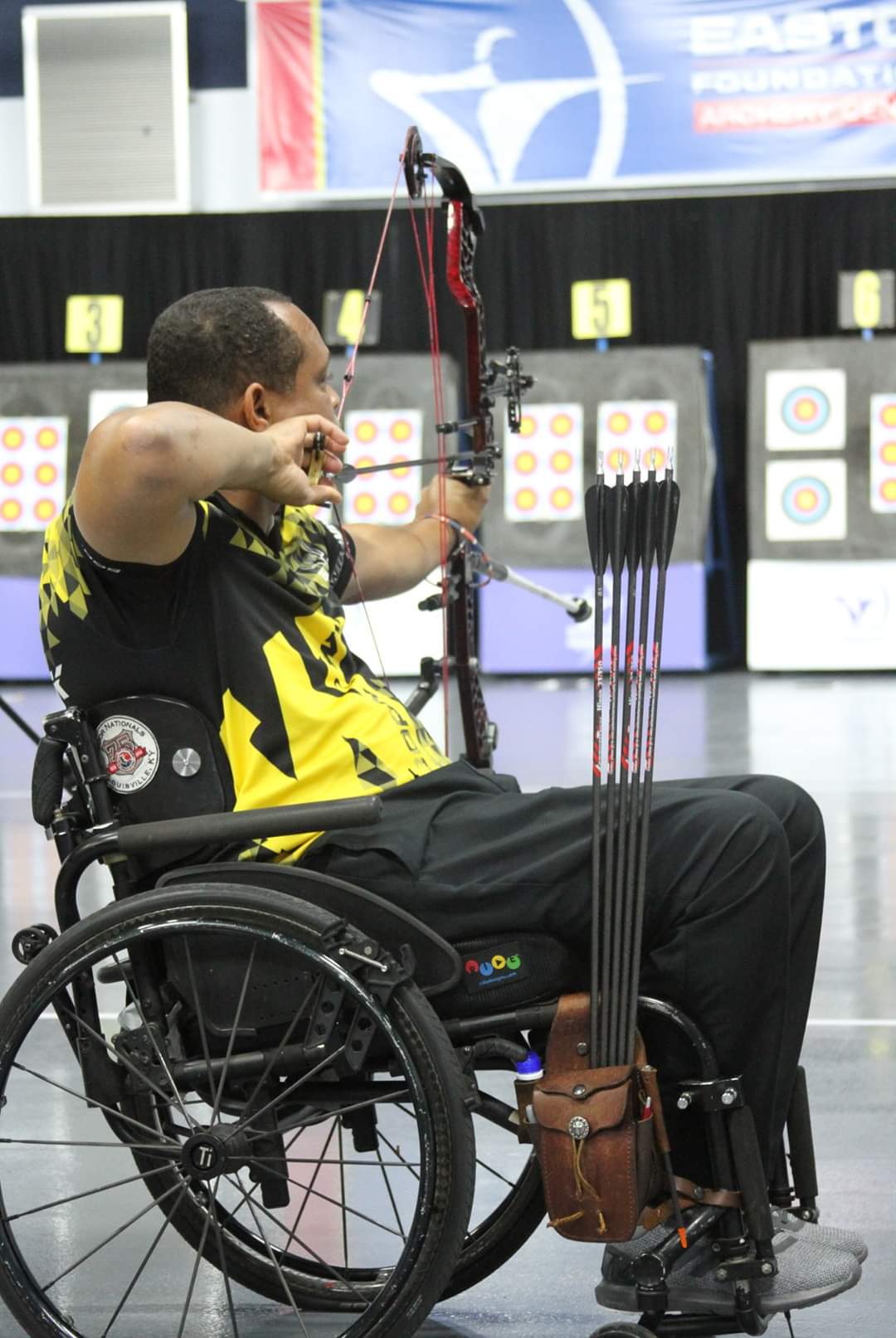 Arhcer in wheelchair drawing back their bow on an indoor range.