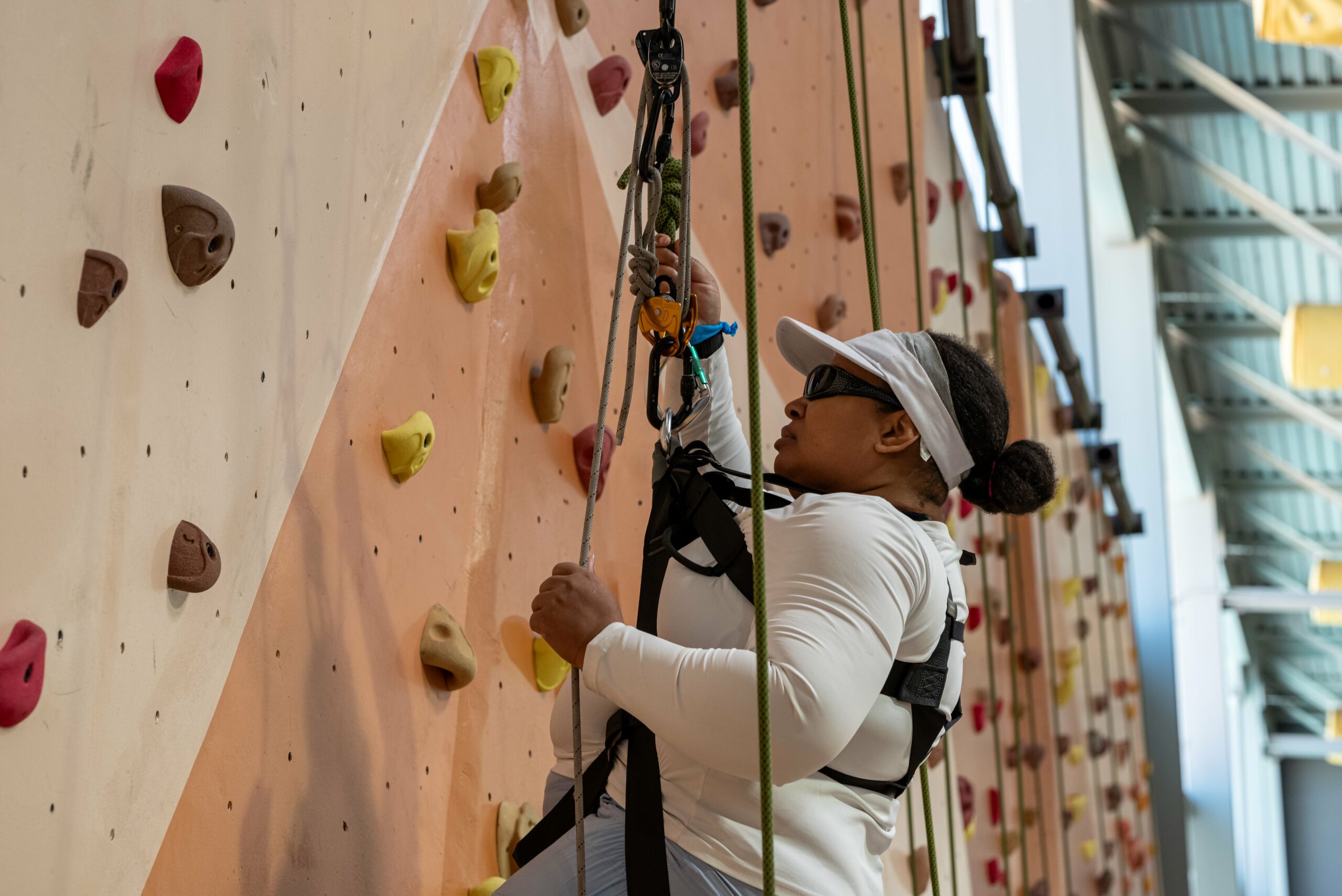Woman in harness on top rope reaching up climbing wall