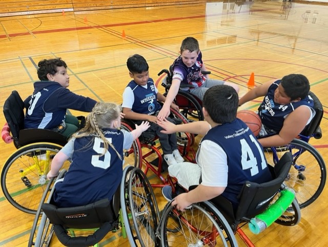 A wheelchair basketball team in a circle with their arms in teh center.