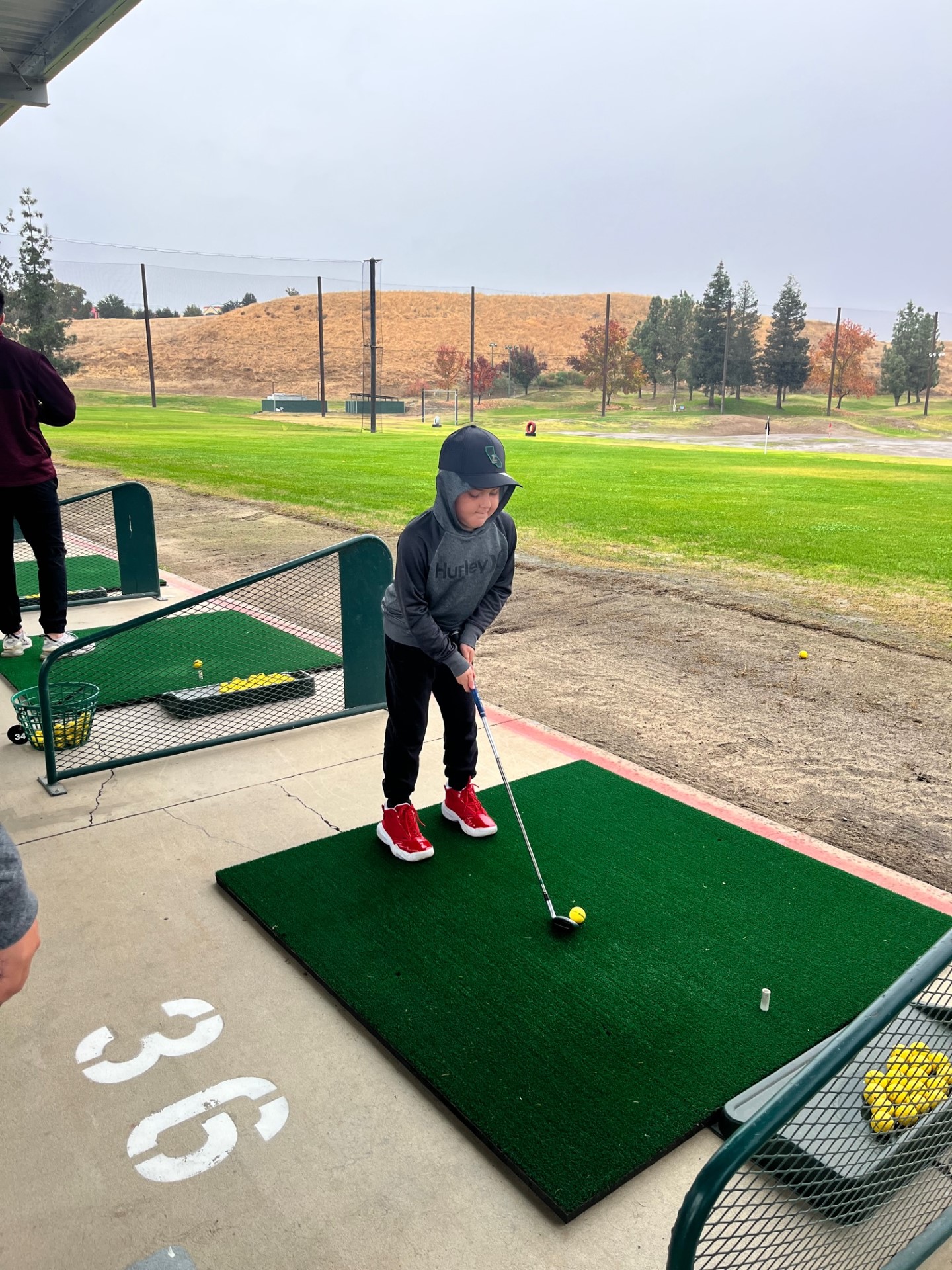 An athlete stands at a golf tee on a range with a golf club in their hand.